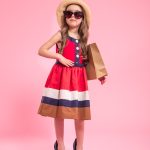 little fashionista with a shopping bag in a summer hat and glasses , on a colored pink background in mom's shoes , the concept of children's fashion